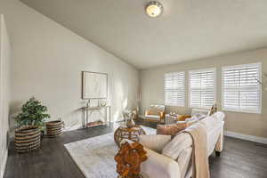 Living room with baseboards, lofted ceiling, a textured ceiling, and hardwood / wood-style flooring