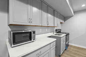 Kitchen with range with electric cooktop, stainless steel microwave, light wood-style floors, light countertops, and baseboards