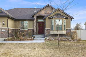 View of front facade with a front yard, fence, roof with shingles, stucco siding, and stone siding