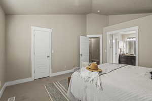Carpeted bedroom with lofted ceiling, visible vents, baseboards, and ensuite bathroom