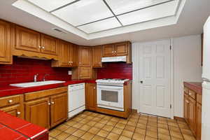 Kitchen featuring visible vents, a sink, under cabinet range hood, tile countertops, and white appliances