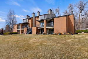 Back of property with brick siding, a balcony, a chimney, and a yard