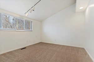 Spare room with baseboards, visible vents, lofted ceiling, rail lighting, and carpet flooring