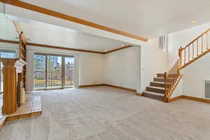 Unfurnished living room featuring carpet flooring, crown molding, stairs, and baseboards