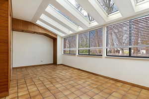 Spare room featuring lofted ceiling with skylight, light tile patterned floors, and baseboards