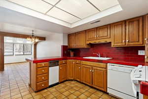 Kitchen with visible vents, tile countertops, dishwasher, brown cabinetry, and a sink