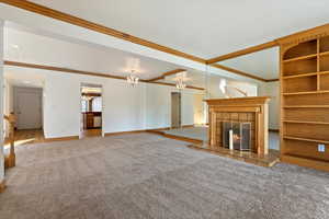 Unfurnished living room with crown molding, baseboards, a tiled fireplace, carpet floors, and a notable chandelier