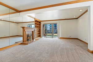 Unfurnished living room with a tiled fireplace, carpet flooring, crown molding, and baseboards