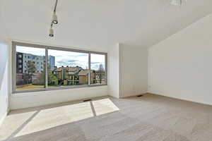 Carpeted empty room with visible vents, baseboards, rail lighting, and vaulted ceiling