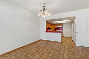 Interior space featuring light tile patterned floors, baseboards, a peninsula, under cabinet range hood, and a raised ceiling