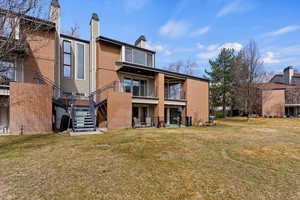 Rear view of house featuring brick siding, stairway, a chimney, and a yard