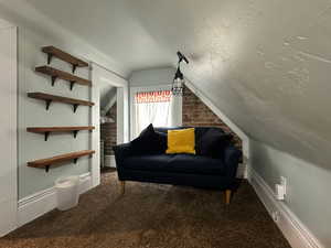 Sitting room featuring lofted ceiling, brick wall, and carpet flooring