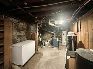 Unfinished below grade area with electric panel, refrigerator, and electric water heater