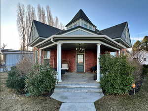 Victorian home with brick siding, covered porch, and roof with shingles