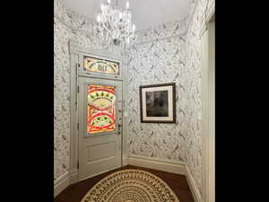Doorway to outside with baseboards, wallpapered walls, and an inviting chandelier