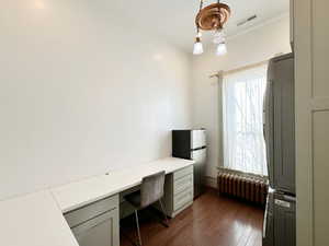 Office area featuring visible vents, dark wood-type flooring, radiator heating unit, built in desk, and stacked washer and clothes dryer