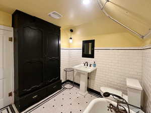 Bathroom with visible vents, wainscoting, and vaulted ceiling