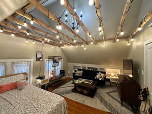 Bedroom with lofted ceiling with beams, rail lighting, and wood finished floors