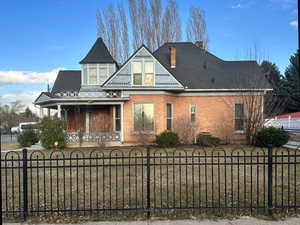 Victorian home featuring a fenced front yard, brick siding, covered porch, and a chimney