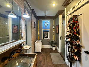 Full bath featuring a stall shower, wood finished floors, brick wall, crown molding, and baseboards