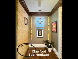 Interior space featuring brick wall, crown molding, baseboards, wood finish floors, and a chandelier