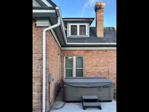 View of home's exterior featuring brick siding, a chimney, and a hot tub