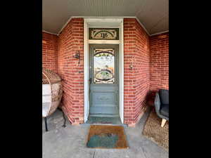 Doorway to property featuring brick siding and covered porch