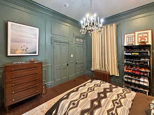 Bedroom with radiator, an inviting chandelier, ornamental molding, dark wood-type flooring, and a decorative wall