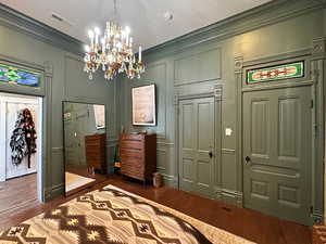 Bedroom featuring visible vents, dark wood-style flooring, crown molding, and a decorative wall