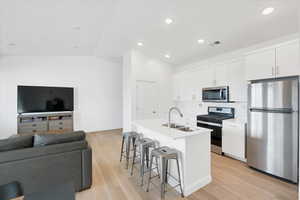 Kitchen with visible vents, vaulted ceiling, appliances with stainless steel finishes, a kitchen breakfast bar, and a sink