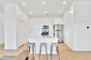 Kitchen featuring an island with sink, recessed lighting, a sink, stainless steel appliances, and light wood-type flooring
