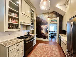 Kitchen featuring decorative light fixtures, dark wood-style floors, appliances with stainless steel finishes, glass insert cabinets, and light stone countertops