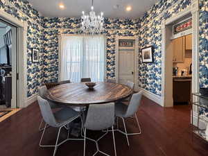 Dining room featuring dark wood finished floors, baseboards, wallpapered walls, and an inviting chandelier