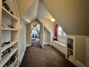 Bonus room featuring baseboards, lofted ceiling, and dark colored carpet