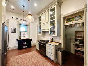 Kitchen with dark wood-style floors, visible vents, stainless steel appliances, decorative backsplash, and glass insert cabinets