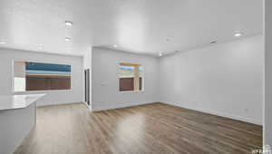 Unfurnished living room with recessed lighting, wood finished floors, baseboards, and a textured ceiling