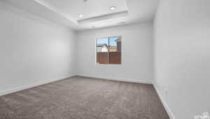 Carpeted empty room featuring a raised ceiling, visible vents, and baseboards