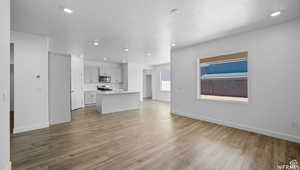 Unfurnished living room featuring recessed lighting, baseboards, a textured ceiling, and wood finished floors