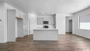 Kitchen featuring dark wood-style floors, visible vents, a kitchen island with sink, light countertops, and appliances with stainless steel finishes