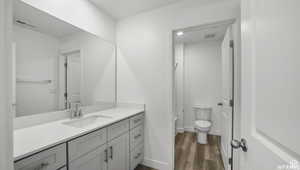 Bathroom featuring visible vents, baseboards, toilet, wood finished floors, and vanity