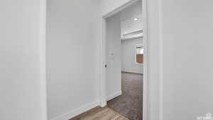 Hallway with light colored carpet, light wood-type flooring, and baseboards