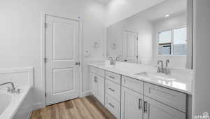 Full bath featuring double vanity, wood finished floors, a garden tub, and a sink