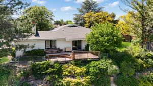 Rear view of property featuring stucco siding, a deck, fence, roof with shingles, and a chimney