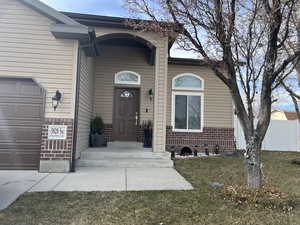 Entrance to property featuring a garage, fence, brick siding, and a lawn