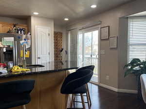 Kitchen with baseboards, a kitchen bar, recessed lighting, stainless steel fridge, and dark wood-style flooring