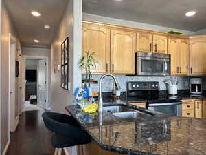 Kitchen featuring a sink, dark stone countertops, backsplash, and stainless steel appliances