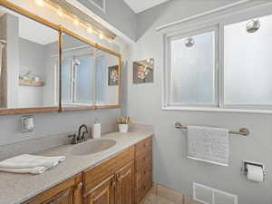 Bathroom with vanity, tile patterned floors, visible vents, and a wealth of natural light