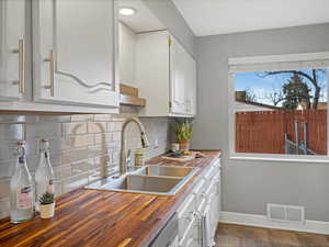 Kitchen featuring visible vents, a sink, white cabinets, backsplash, and butcher block counters