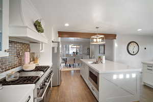 Kitchen with wood finished floors, premium range hood, appliances with stainless steel finishes, and a sink