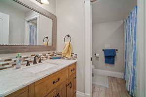 Bathroom featuring vanity, wood finished floors, baseboards, decorative backsplash, and toilet